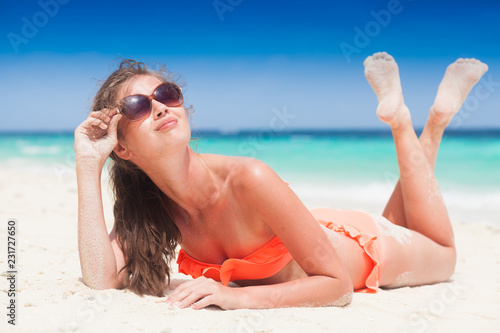 portrait of long haired woman in red swimsuit and sunglasses lying on tropical beach. Maldives