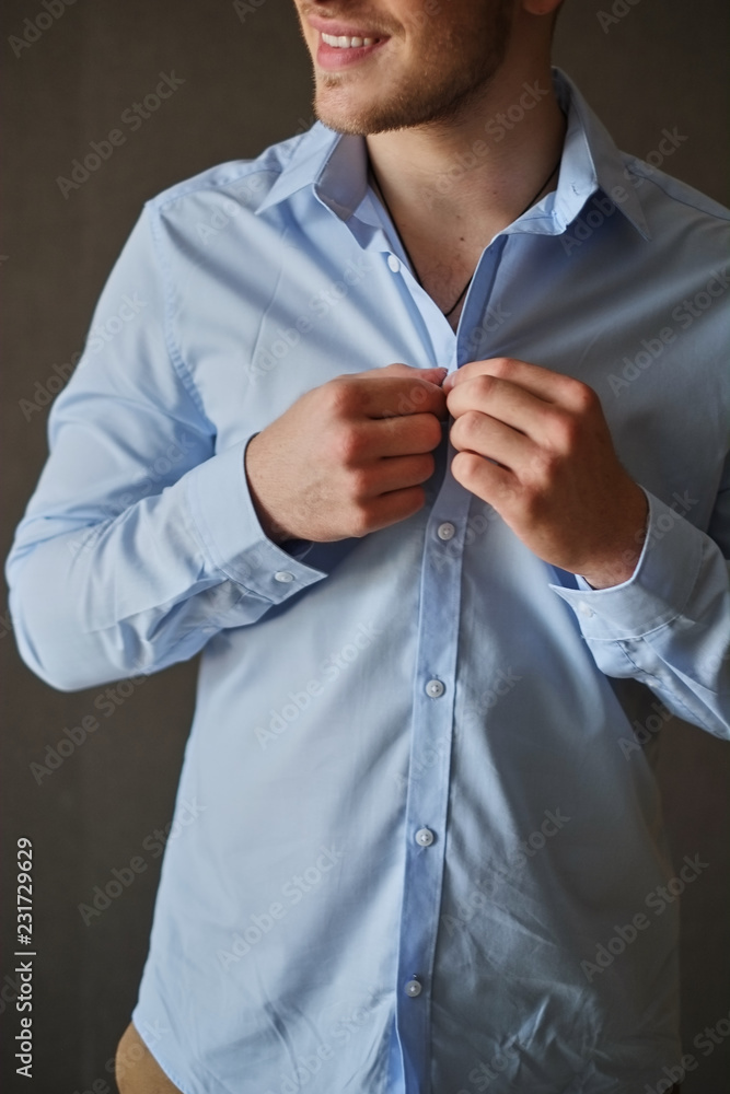 Man adjusting his shirt buttons. man in a blue shirt wears buttoning buttons on a gray background