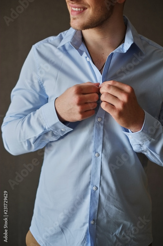 Obraz na płótnie Man adjusting his shirt buttons. man in a blue shirt wears buttoning buttons on a gray background w salonie
