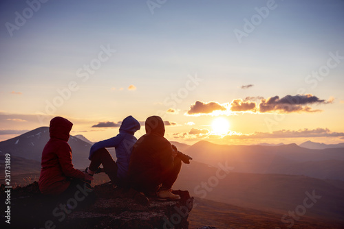 Three friends sits mountains top sunset view