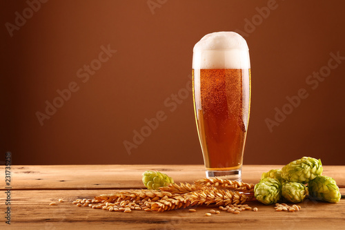 Close up beer glass, hops and barley over brown