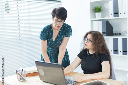 Business people, technology and communication concept - Mid-aged lady helping her female colleague with a laptop © satura_