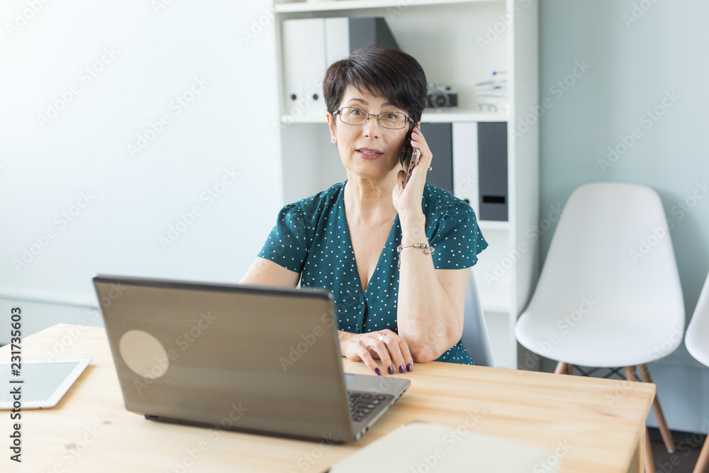 Office and business people concept - Middle aged woman at office working with laptop and making a phone call Office and business people concept - Middle aged woman at office working with laptop and making a phone call