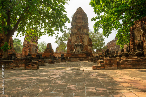 Alley with ancient destroyed Buddha statues, big sculpture and brick pagoda in famous siam temple Wat Mahathat in historical park Ayutthaya, Thailand