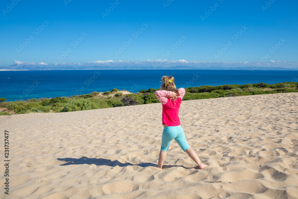 little girl practicing yoga on dune with Africa on the horizon