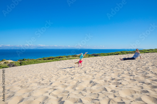 little girl doing handstand on sand next to mother