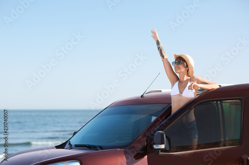 Young woman in straw hat near car on beach