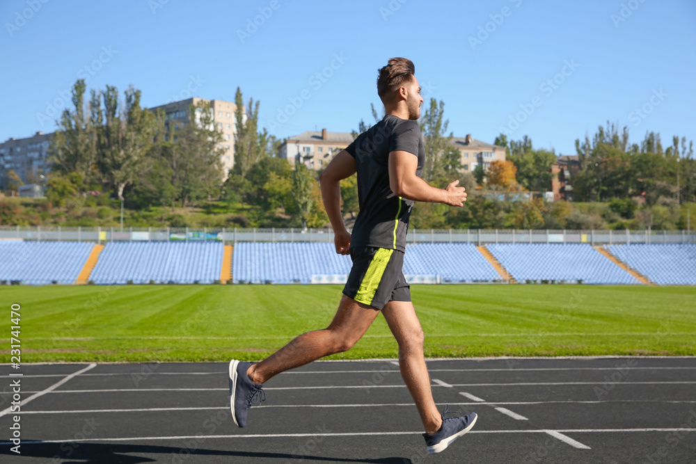Sporty man running at stadium on sunny morning
