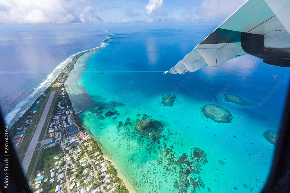 Fototapeta premium Tuvalu lagoon under wing of an airplane. Aerial view of Funafuti atoll and the airstrip of International airport in Vaiaku. Fongafale motu. Island nation in Polynesia, South Pacific Ocean, Oceania.