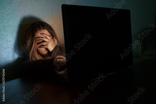 Teenager girl suffering internet cyber bullying scared and depressed cyberbullying. Image of despair girl humilated on internet by classmate. Young teenage girl crying in front of the laptop