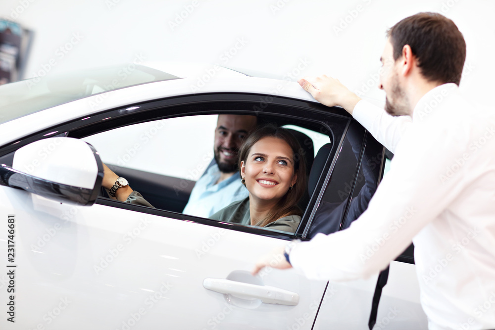 Confident young salesman explaining car features to the young attractive owners Confident young salesman explaining car features to the young attractive owners