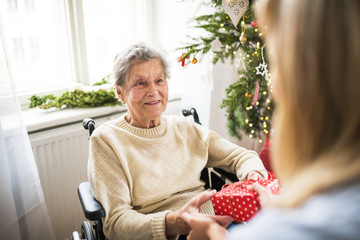 Health visitor and senior woman in wheelchair with a present at home at Christmas.