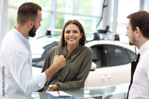 Confident young salesman explaining car features to the young attractive owners