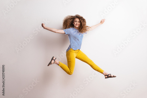 Young beautiful joyful woman with long curly hair in studio, jumping.
