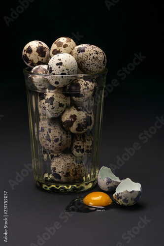 Quail eggs in a glass with one broken egg on a black background photo