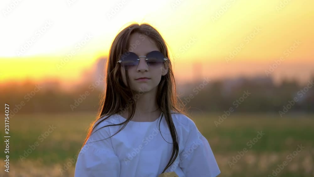 close up pretty little girl puts on sunglasses and playing the guitar in outdoor at sunset. emotions and funnier grimaces imitate pop artists. live performance in nature close up pretty little girl puts on sunglasses and playing the guitar in outdoor at sunset. emotions and funnier grimaces imitate pop artists. live performance in nature