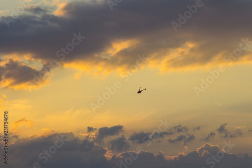 Sunset on the background of turquoise sky - golden rays of the sun, dark clouds and flying helicopter