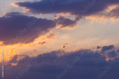 Sunset on a blue sky background - golden rays of the sun, dark-pink clouds and a flying helicopter