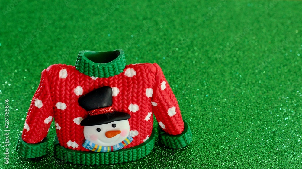red sweater with green collar and sleeve cuffs white snowflakes and snowman with black hat and carrot nose on a festive green background  with copy space