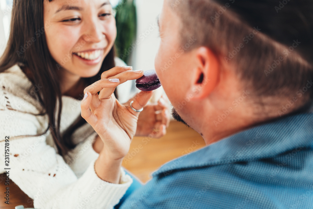 Happy couple having fun together girl feeding man with sweet cookies. Multiethnic young family Happy couple having fun together girl feeding man with sweet cookies. Multiethnic young family