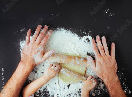 Top view of fathers and kids hands rolling the dough on black background