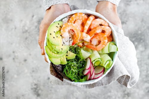 Foto Girl holding shrimp poke bowl with seaweed, avocado, cucumber, radish, sesame seeds