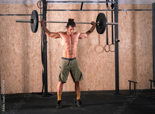 Strong young man lifting bar with weight in the gym