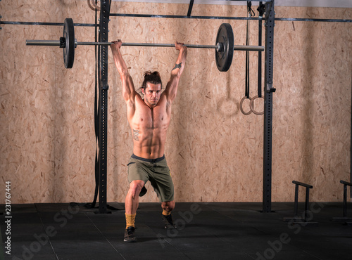 Strong young man lifting bar with weight in the gym