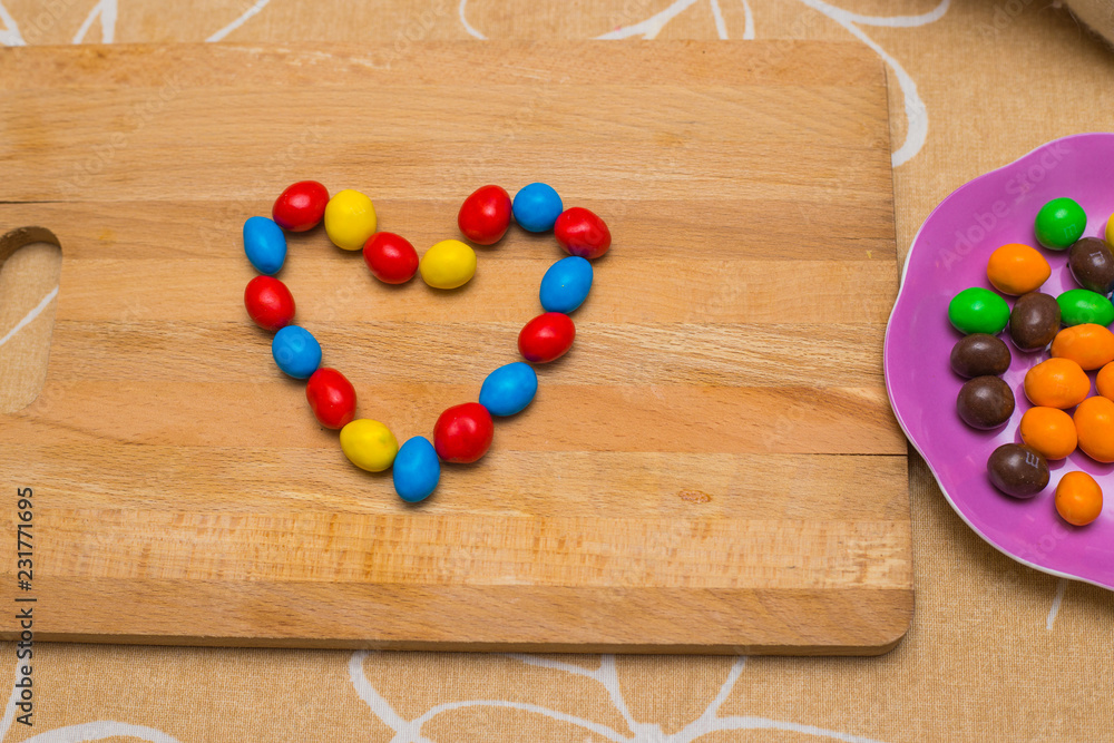Colorful chocolate candyes lying on the table the shape of heart and some candyes nearby in the saucer Colorful chocolate candyes lying on the table the shape of heart and some candyes nearby in the saucer
