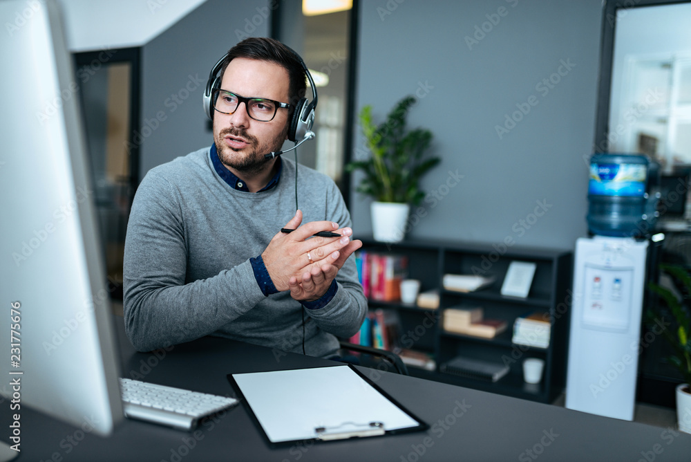 Attractive male support center agent with headset on talking to client. - obrazy, fototapety, plakaty 