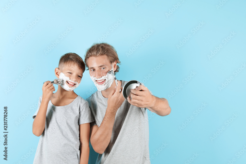 Father and son shaving together on color background, space for text Father and son shaving together on color background, space for text