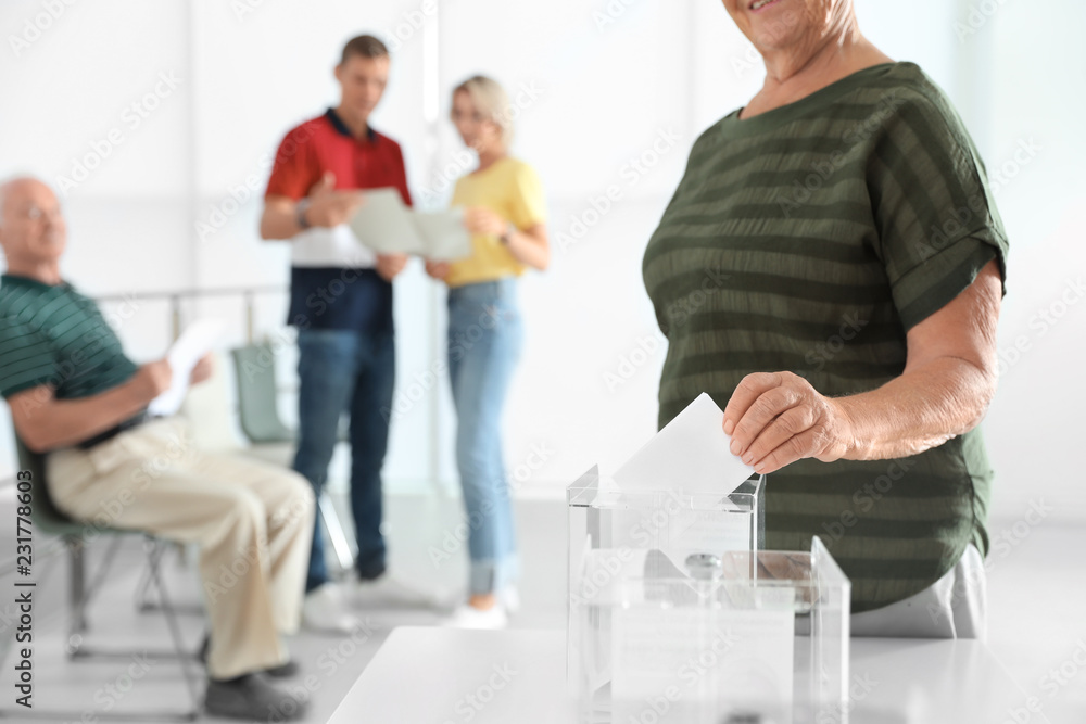 Fototapeta premium Elderly woman putting ballot paper into box at polling station