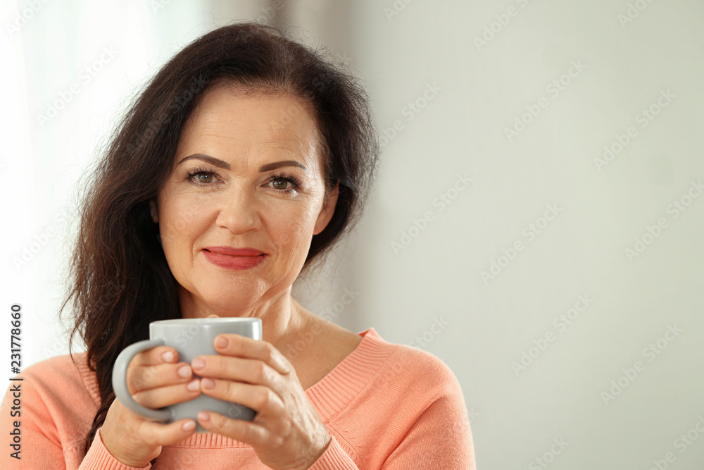 Portrait of beautiful older woman with cup of tea against blurred background. Space for text Portrait of beautiful older woman with cup of tea against blurred background. Space for text