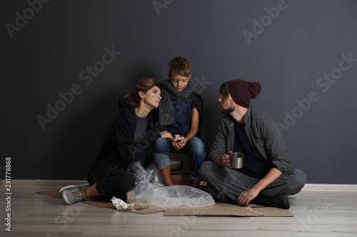 Poor homeless family sitting on floor near dark wall