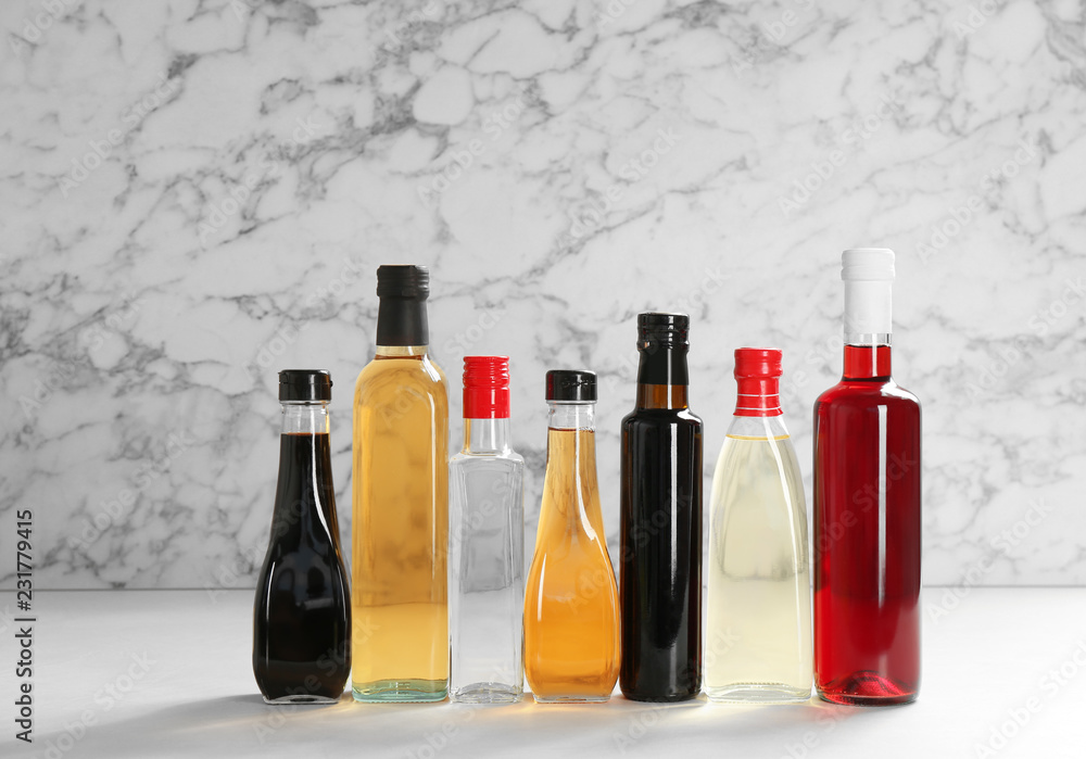 Bottles with different kinds of vinegar on table against marble background