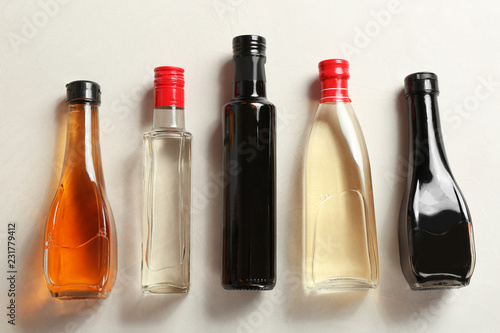 Bottles with different kinds of vinegar on light table, top view