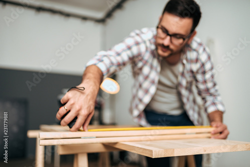 Young man working on a DIY project measuring wood. Focus on the foreground.
