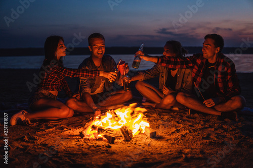 Camp on the beach. Group of young friends having picnic with bonfire and drinking together. Cheers