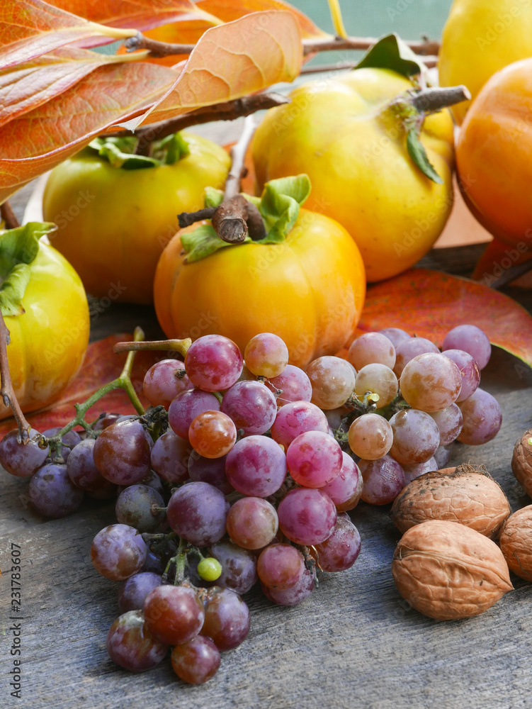 persimmons, grapes, quince and walnuts on a rustic wooden table with leaves, vertical persimmons, grapes, quince and walnuts on a rustic wooden table with leaves, vertical