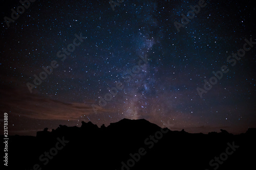 The Milky Way appears to erupt from a peak silhouetted against a starry sky in the Bisti Badlands of New Mexico