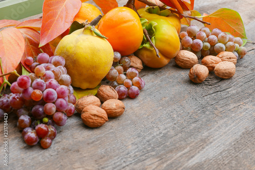 persimmons, grapes, and walnuts with branches and orange foliage on a rustic wooden table with copy space