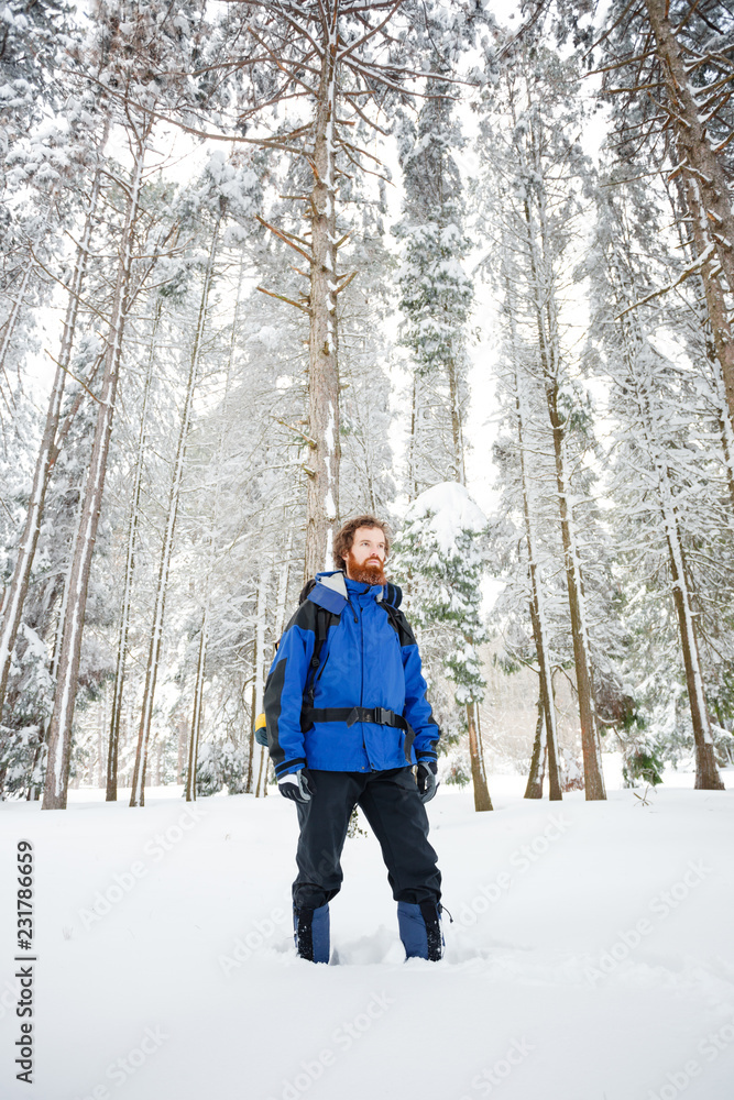 Bearded young mountain climber standing in deep powder snow, surrounded by tall fir trees. Wide angle front view Bearded young mountain climber standing in deep powder snow, surrounded by tall fir trees. Wide angle front view