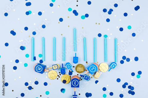 Blue confetti background with menora made of dreidels and chocolate coins. Hanukkah and judaic holiday concept.