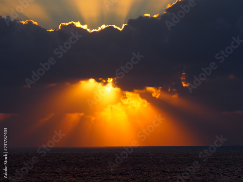 dramatic sunset over the sea with rays of light emerging from dark illuminated clouds over a calm ocean