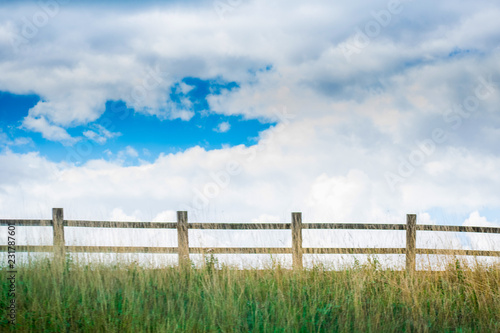 Closeup of very beautiful landscape view with Wooden fence in a green field against blue cloudy sky .