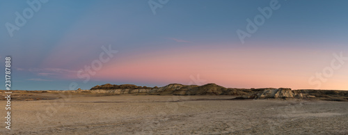 Panorama of the desert landscape and hills of the Bisti Badlands of New Mexico at sunset under a beautiful dramatic sky with blue, pink, peach, and purple hues