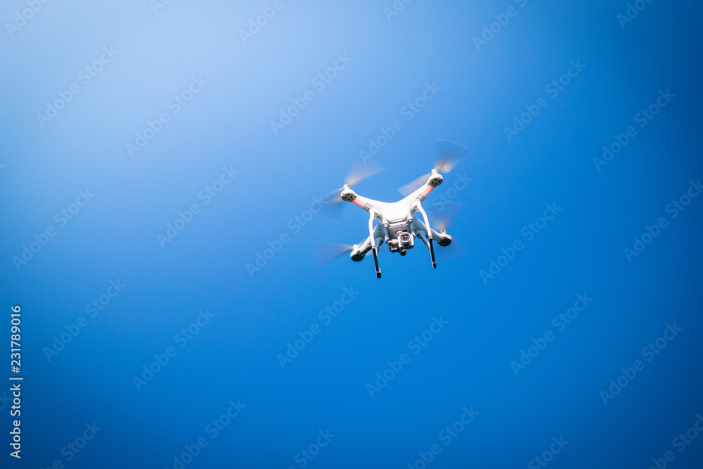 Closeup of white camera drone flying with visible propellers movement in  blue sky background with no clouds
