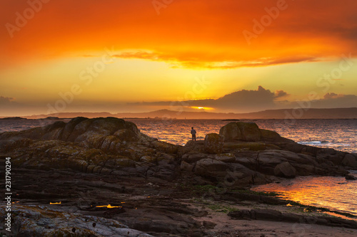 Angler on coastal rocks at sunset