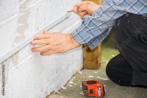 Closeup of worker man using a spirit level and marking the wall with a pencil to fix it