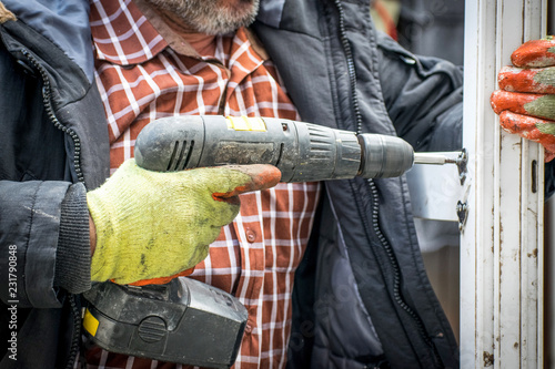Closeup of Man wearing green gloves and Using a Power electric Drill screws and install a door using an electric drill at home in a clod winter day